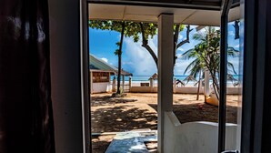 A view from inside a building to a beach area with palm trees and a thatched-roof structure.
