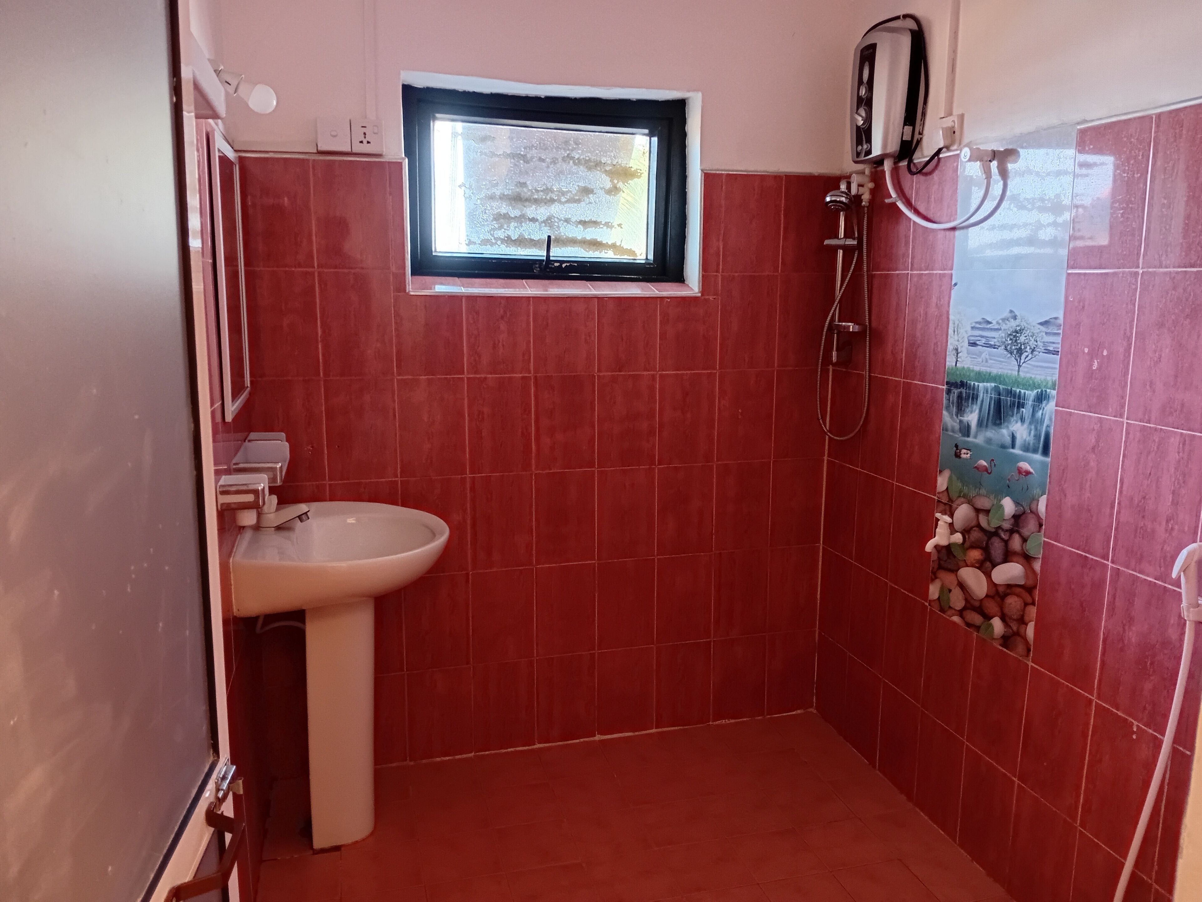Un baño con baldosas rojas, una ventana, un lavabo y una ducha.