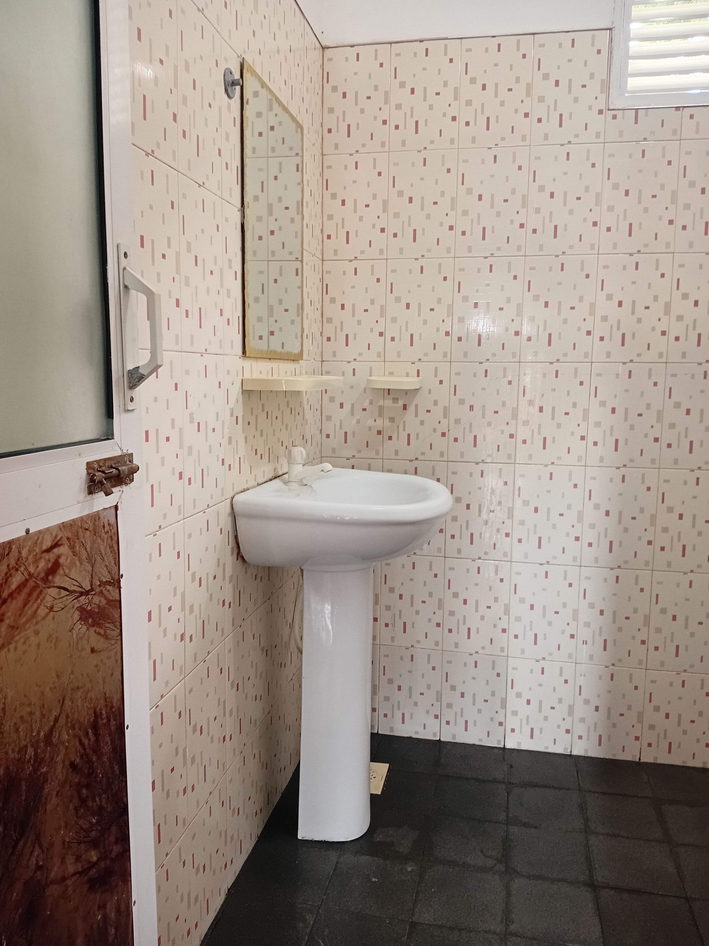 A bathroom with a white pedestal sink, a mirror above it, and patterned tiles on the walls and floor.