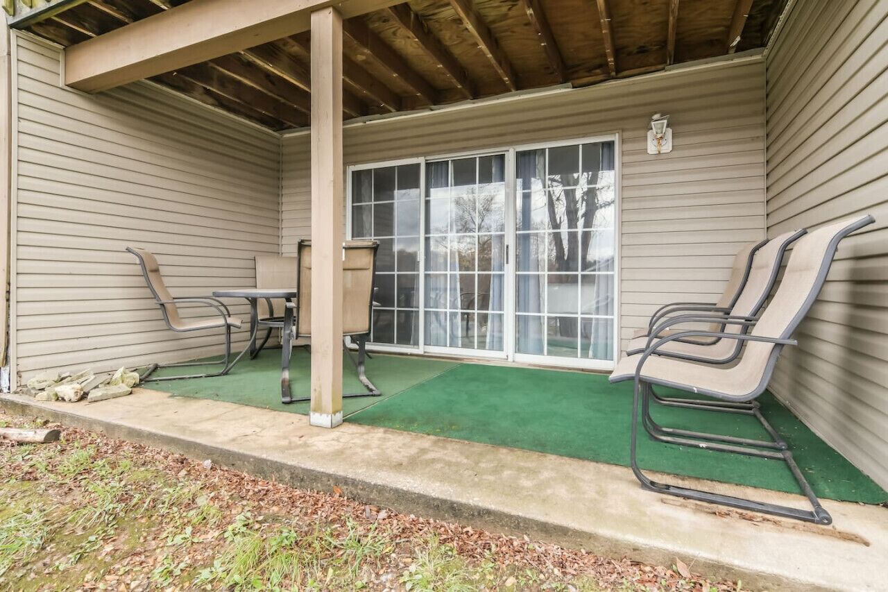 A covered patio with a table and chairs, a sliding glass door, and a green carpet.