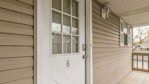 A white door with the number 6, a small porch with a railing, and a window with shutters.
