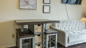 A living room with a white tufted sofa, a small table with storage baskets, and framed artwork on the wall.
