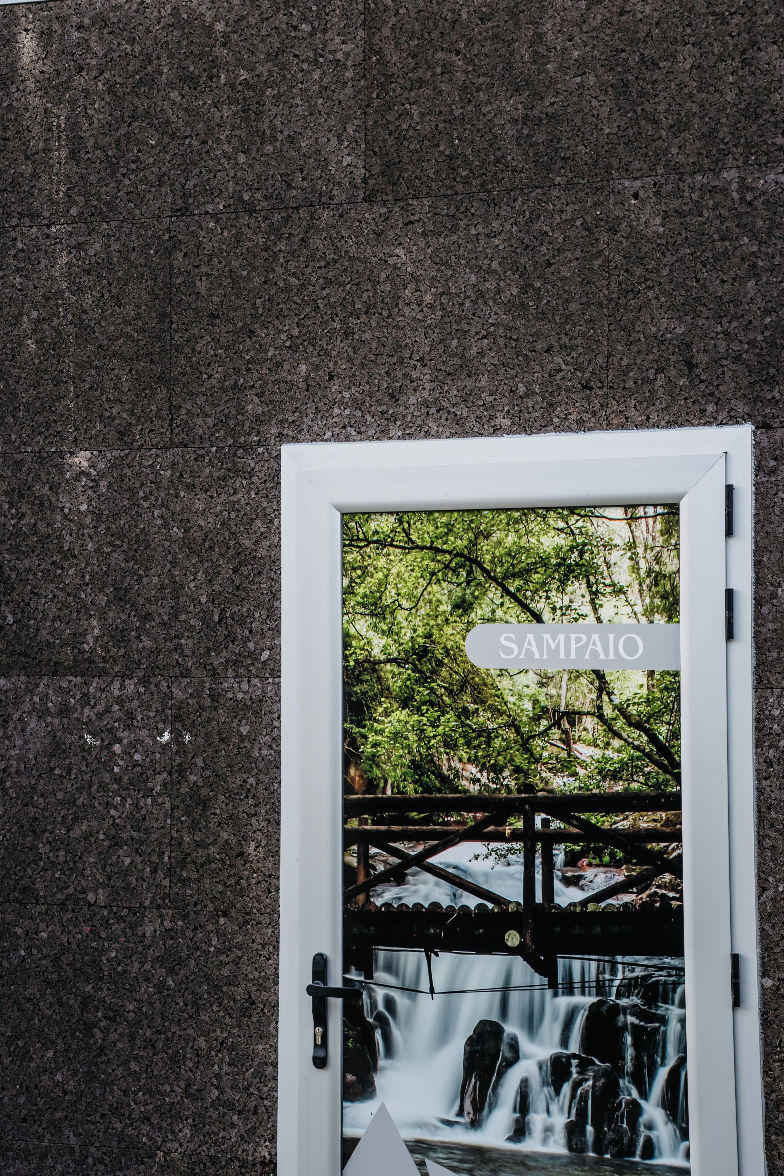 A door with a sign that reads "SAMPALCO" and a view of a waterfall through the door.
