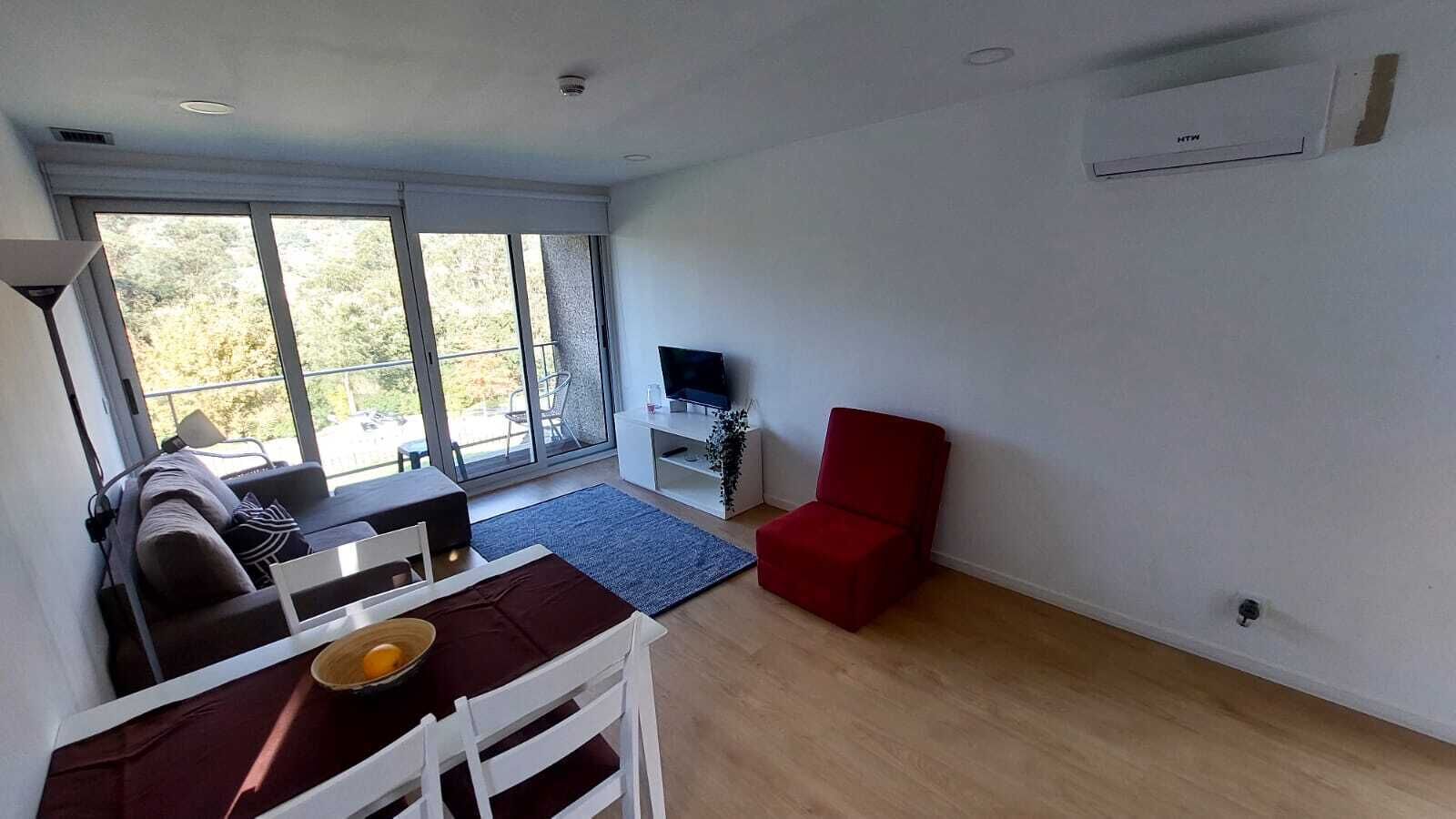 En moderne stue med sofa, rød lænestol, fjernsyn og et spisebord med stole.