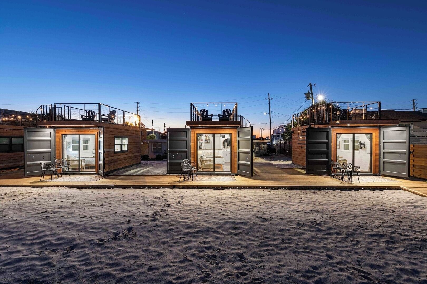 Una hilera de casas de playa modernas y compactas, cada una con puertas de vidrio correderas y un pequeño patio con sillas.