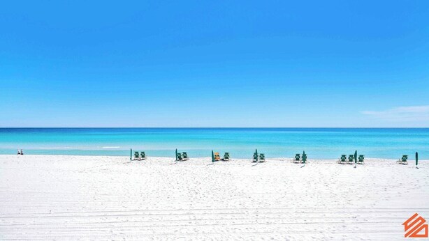 A beach with white sand and a clear blue sky. There are several green lounge chairs aligned in rows. - Beachside Container Tiny Home Saltwater Oasis (Fort Walton Beach)