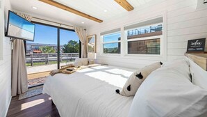 A spacious bedroom with a large bed, a TV, and a balcony with a view of the beach. - Beachside Container Tiny Home Saltwater Oasis (Fort Walton Beach)