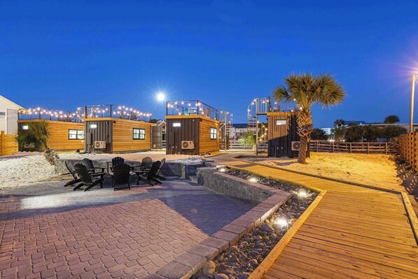 A beachfront property with wooden cabins, outdoor seating, and a wooden deck.