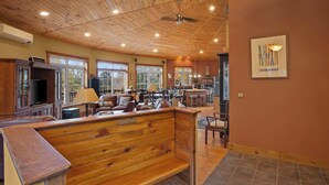 Amplia sala de estar con techo de madera, un banco grande de madera y un comedor con mesa y sillas.