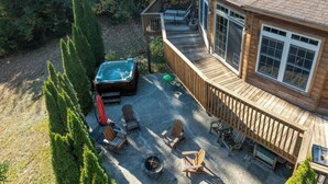 Una terraza de madera con jacuzzi, mobiliario exterior y vistas del bosque circundante.