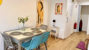 Een eethoek met een tafel, stoelen, een vaas met bloemen, een schilderij, een bureau met een lamp en een brandblusser.
