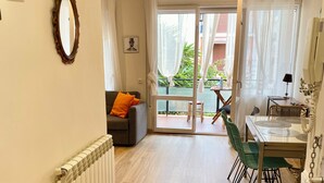 Een ruime woonkamer met een bank, een eettafel met stoelen, een rieten mand en een radiator.