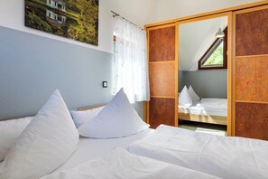 A bedroom with a bed, white pillows, a large mirror, and a window with curtains.