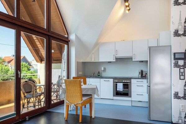 A modern kitchen with white cabinets, a stainless steel oven, and a dining area with wicker chairs.