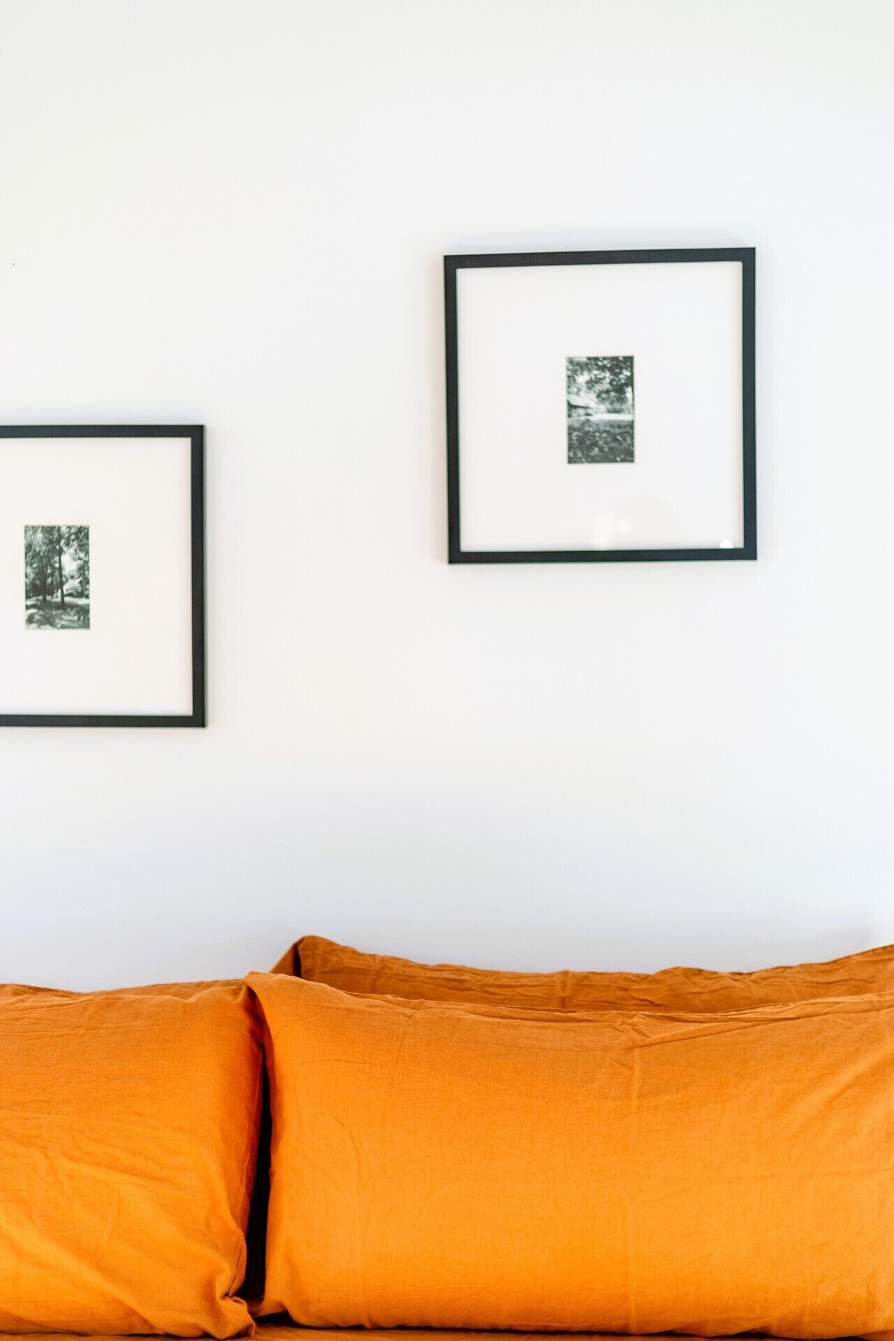 Een kamer met een witte muur, twee ingelijste foto's en een mosterdgele bank.