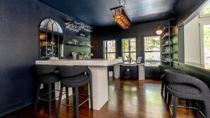 A modern bar area with a bar counter, stools, and a hanging light fixture.