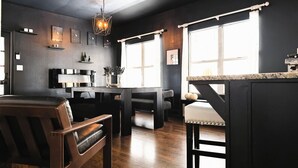 A modern kitchen with dark walls, wooden flooring, and a central island. There are bar stools and a dining table with chairs.