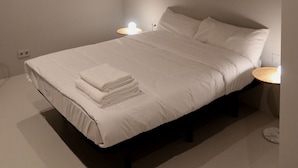 Un dormitorio minimalista con cama, lámparas de noche e iluminación empotrada en el techo.