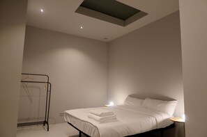 Un dormitorio moderno con una cama bien tendida, un perchero y una mesita de noche con una lámpara.