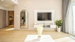 Ein modernes Wohnzimmer mit einem großen Flachbildfernseher, der an einer weißen Konsole befestigt ist, einem großen Spiegel und einem Topfpflanzen.