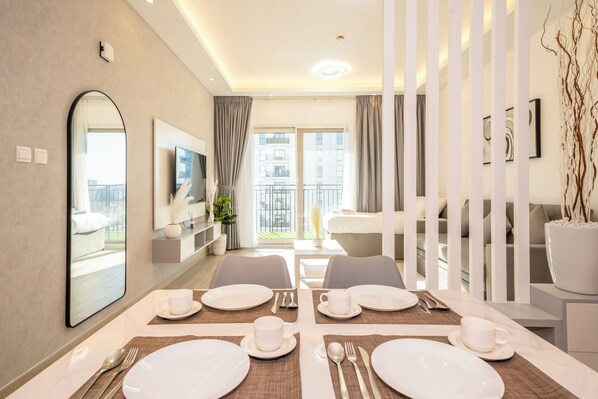 Quarto de hotel moderno com área de jantar para quatro pessoas, um espelho grande, televisão e varanda com vista para edifícios.
