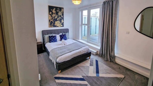 Une chambre à coucher avec un lit, une fenêtre avec des rideaux, un luminaire au plafond et une œuvre d’art accrochée au mur.