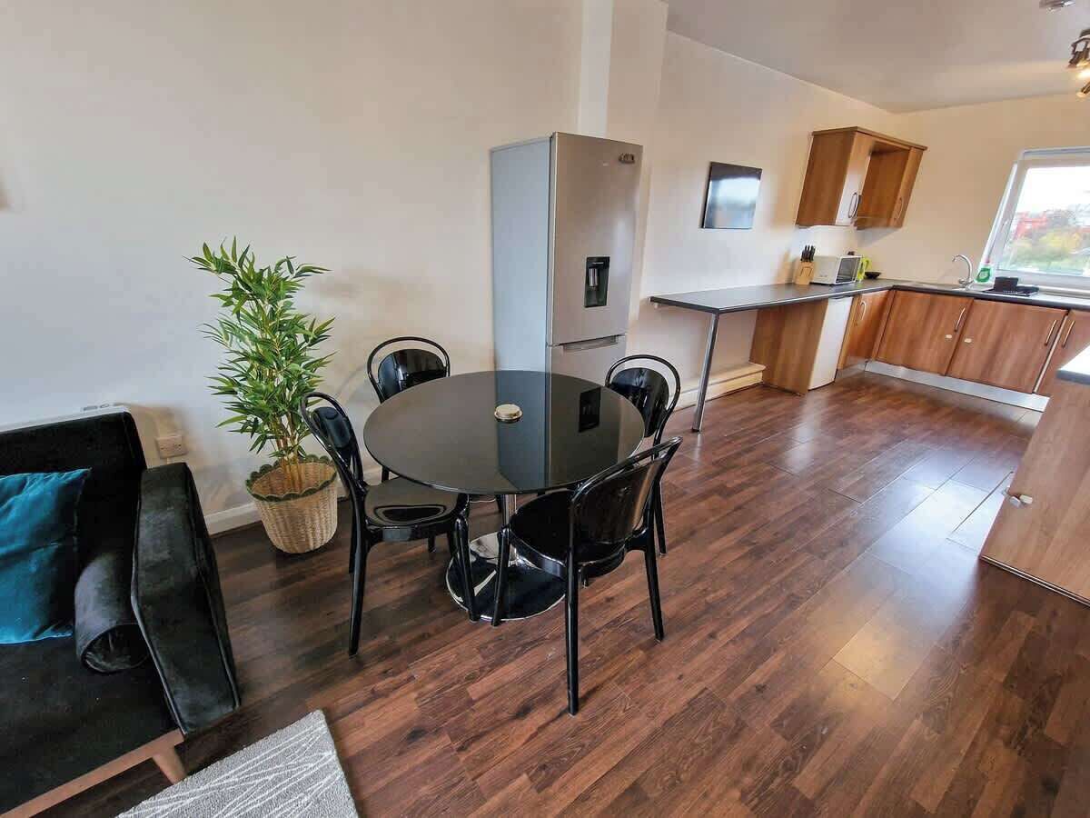 A modern kitchen with a built-in oven, a dining area with a round table and chairs, a potted plant, and a view of the outside through a window.