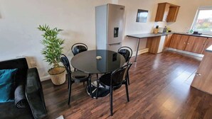 Une cuisine moderne dotée d’un four encastré, un coin repas avec une table ronde et des chaises, une plante en pot et une vue sur l’extérieur par une fenêtre.