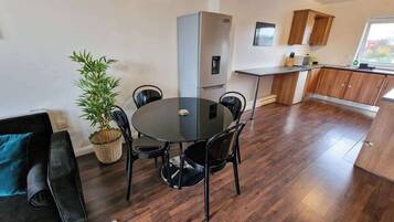 A modern kitchen with a built-in oven, a dining area with a round table and chairs, a potted plant, and a view of the outside through a window.