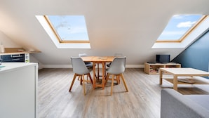 A modern loft apartment with skylights, a dining table, chairs, a sofa, and a TV.
