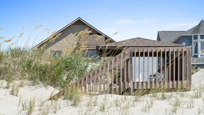 Ein Strandhaus mit einer Holzterrasse und einem sandigen Strand im Vordergrund.