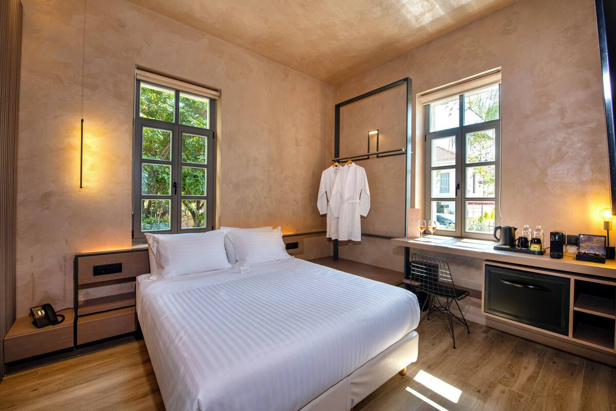 Ein modernes Hotelzimmer mit einem großen Bett, Nachttischen, einem Schreibtisch mit Stuhl und einem Fenster mit Blick auf Grünflächen.