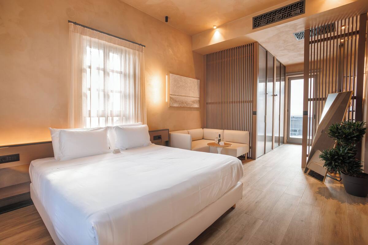 Ein modernes Hotelzimmer mit einem großen Bett, einem Schlafsofa, einem kleinen Tisch und einer Zimmerpflanze.