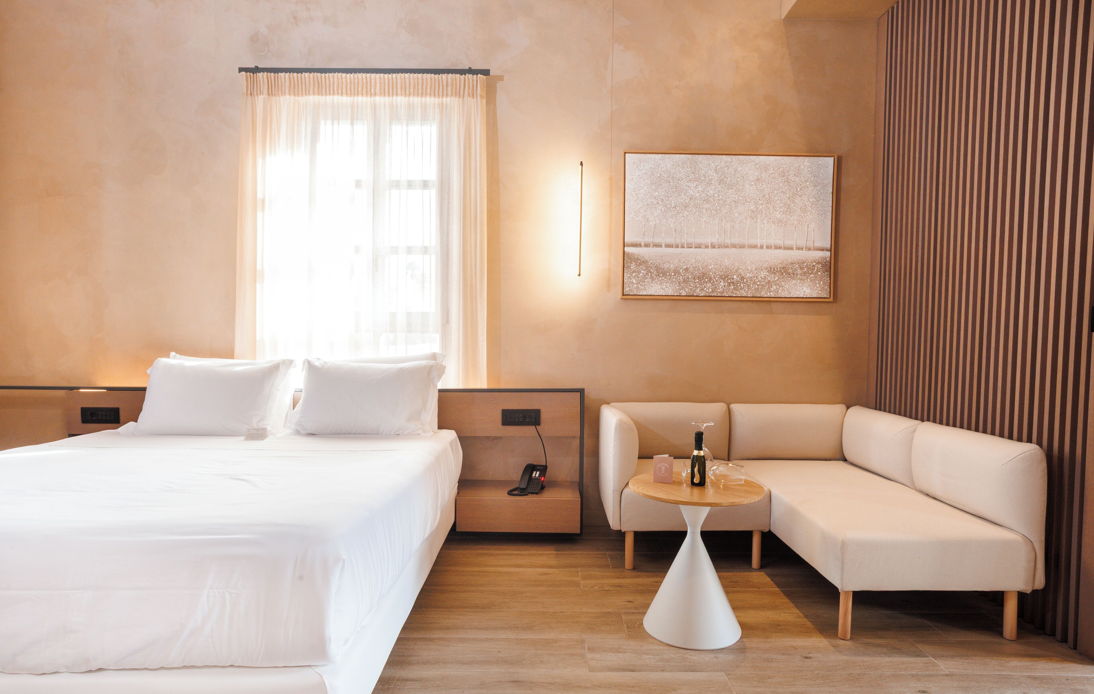 A modern hotel room with a large bed, a sofa, a small table, and a painting on the wall.