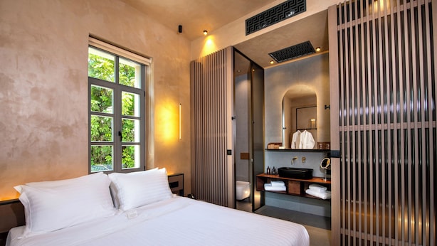 A modern hotel room with a large bed, a bathroom with a vanity, and a view of greenery through the window. - Nearchou Boutique Hotel (Chania)