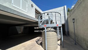 A modern building with a covered parking area, a metal staircase, and a cylindrical tank.