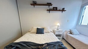 A bedroom with a bed, bedside tables, a lamp, and two shelves with items on the wall.