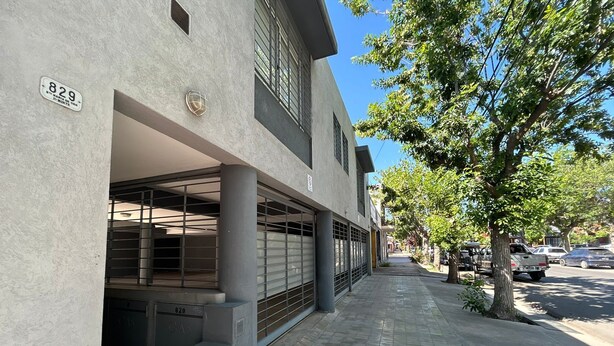 A building with a garage entrance, a gas meter, and a street with parked cars and trees.