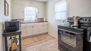 A kitchen with white cabinets, a black stove, and a window with blinds. - The Loft - 1BR/1BA - Close to TTU (Lubbock)