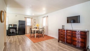 A compact kitchen with a refrigerator, stove, and oven, a dining area with a table and chairs, and a wooden dresser with drawers. - The Loft - 1BR/1BA - Close to TTU (Lubbock)
