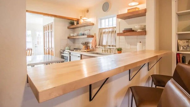 Una cocina moderna con una encimera amplia, estanterías de madera y un comedor con sillas.