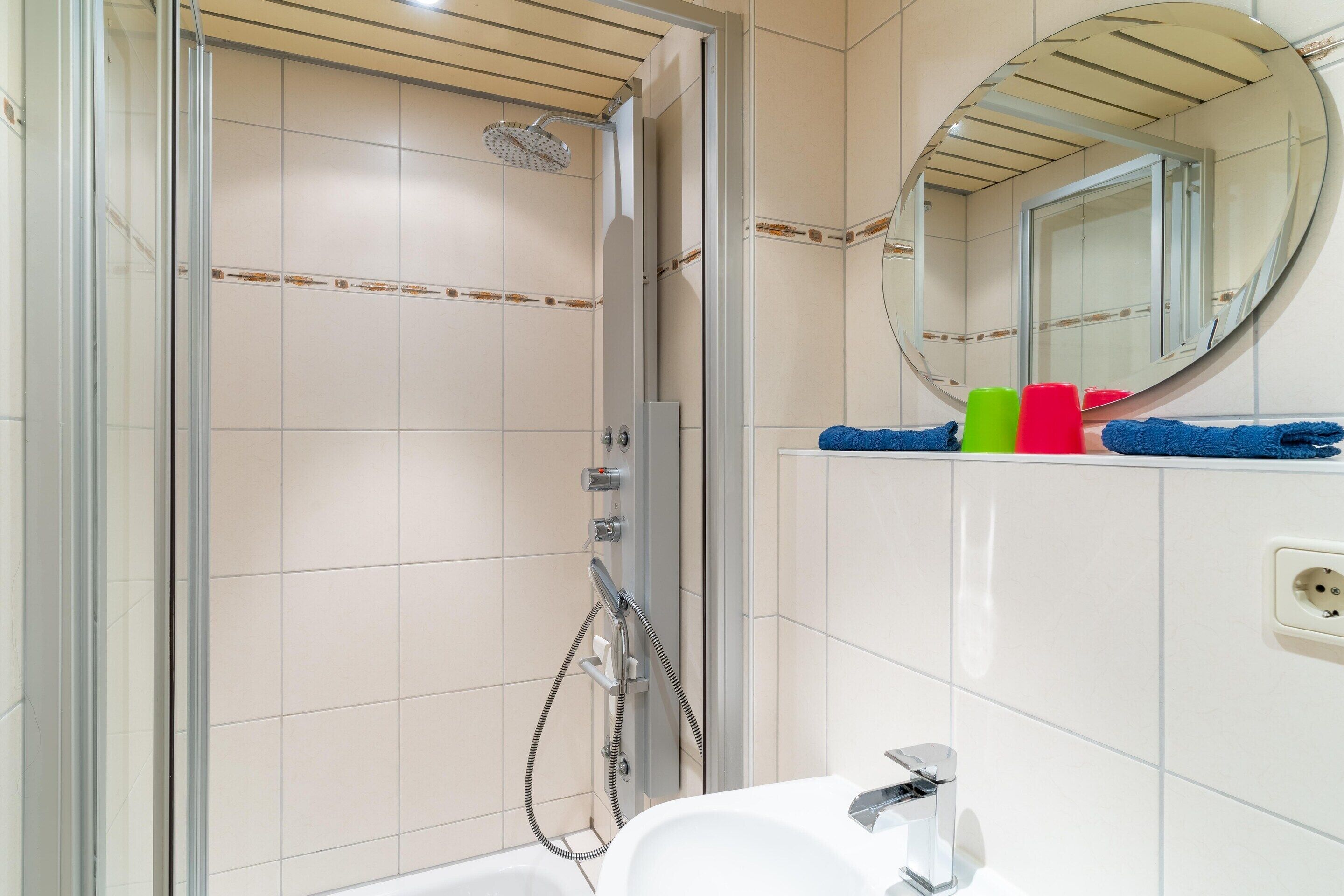 Un baño con ducha envuelta en vidrio, un lavabo blanco y un espejo con marco redondo.