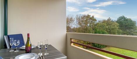 A balcony with a table set for two, a bottle of wine, and a scenic view of trees and sky.