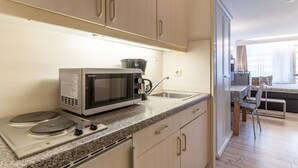 A compact kitchen with a microwave, stove, and sink. There is a dining area with a table and chairs visible through an open door. - Ferienwohnung in St. Peter-ording (St. Peter-Ording)