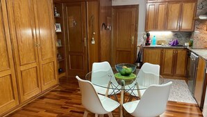 A kitchen with wooden cabinets, a glass dining table with white chairs, and a green bowl on the table. - Beautiful studio, fully equipped.   (La Molina)