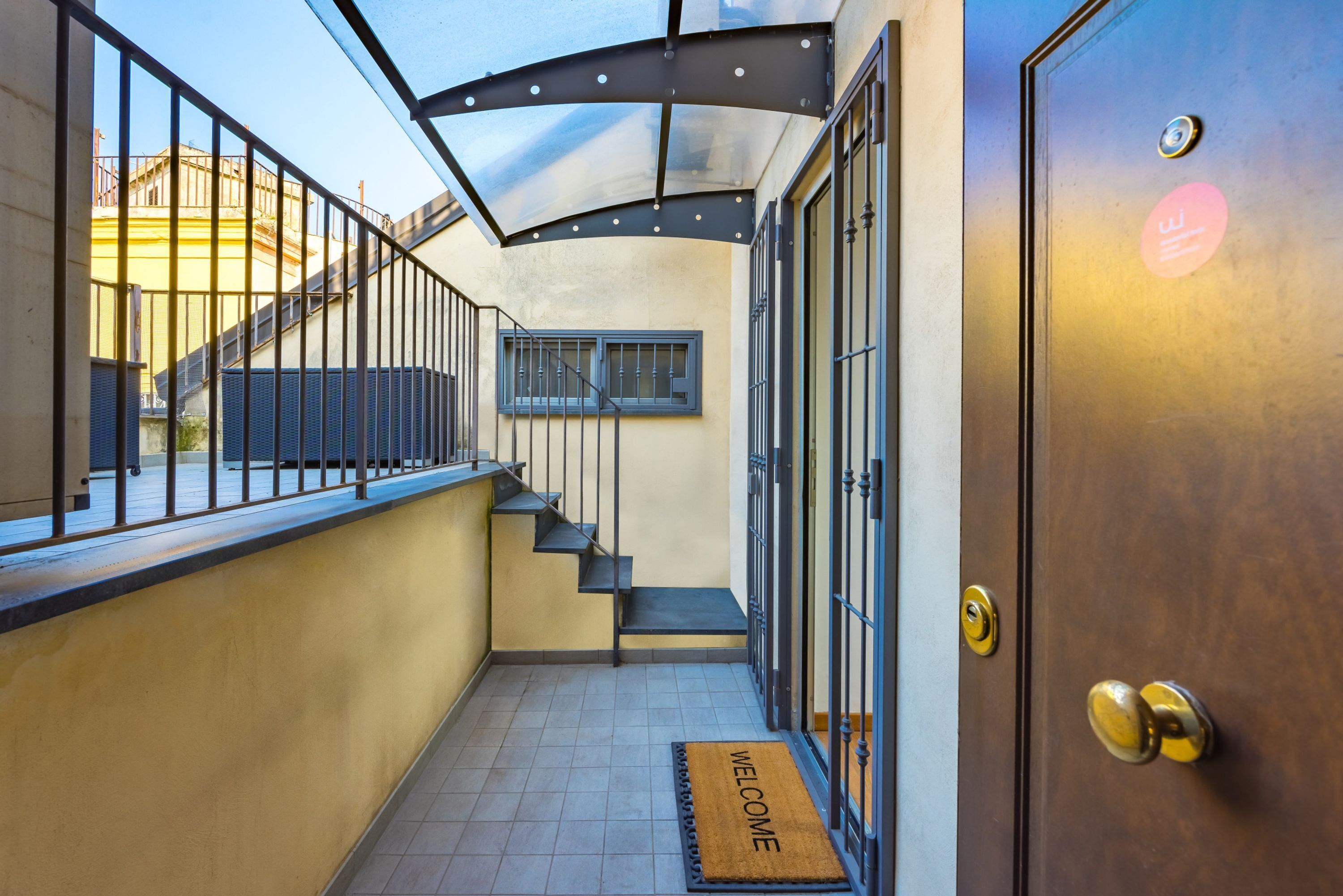 A narrow hallway with a metal railing, a wooden door, and a welcome mat.