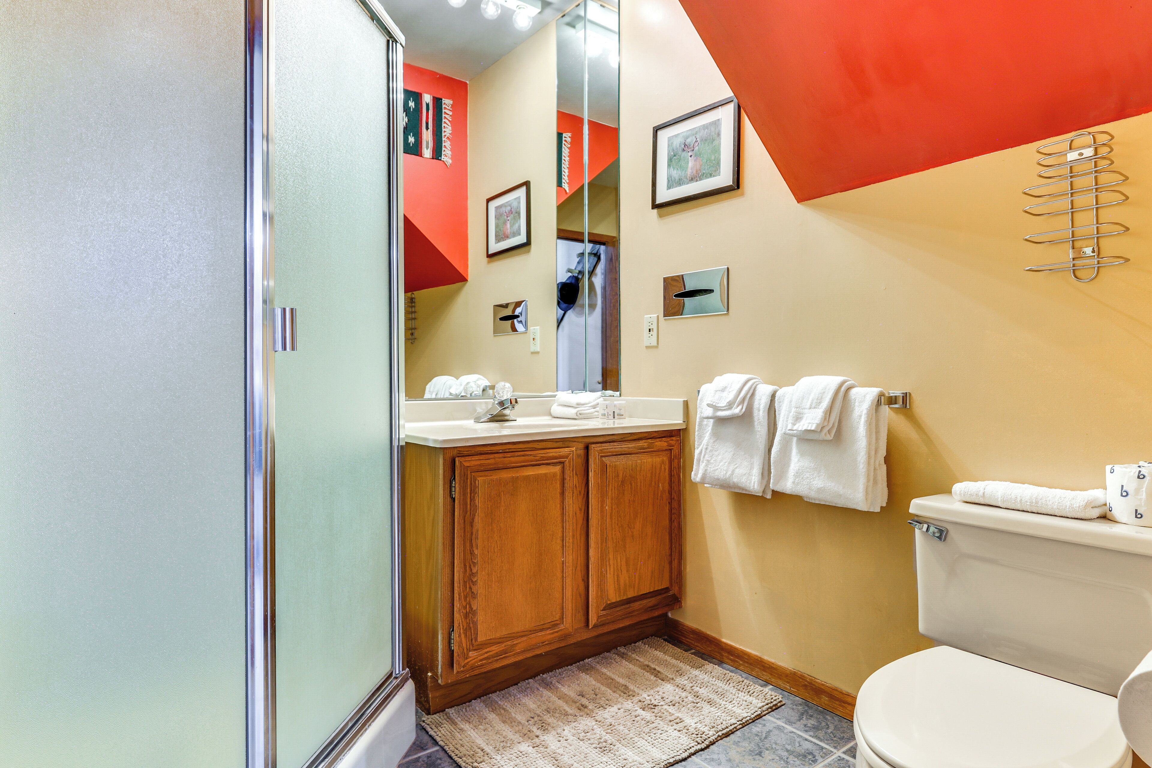 Un baño con ducha, un lavabo con espejo, inodoro y toallas colgadas en la pared.
