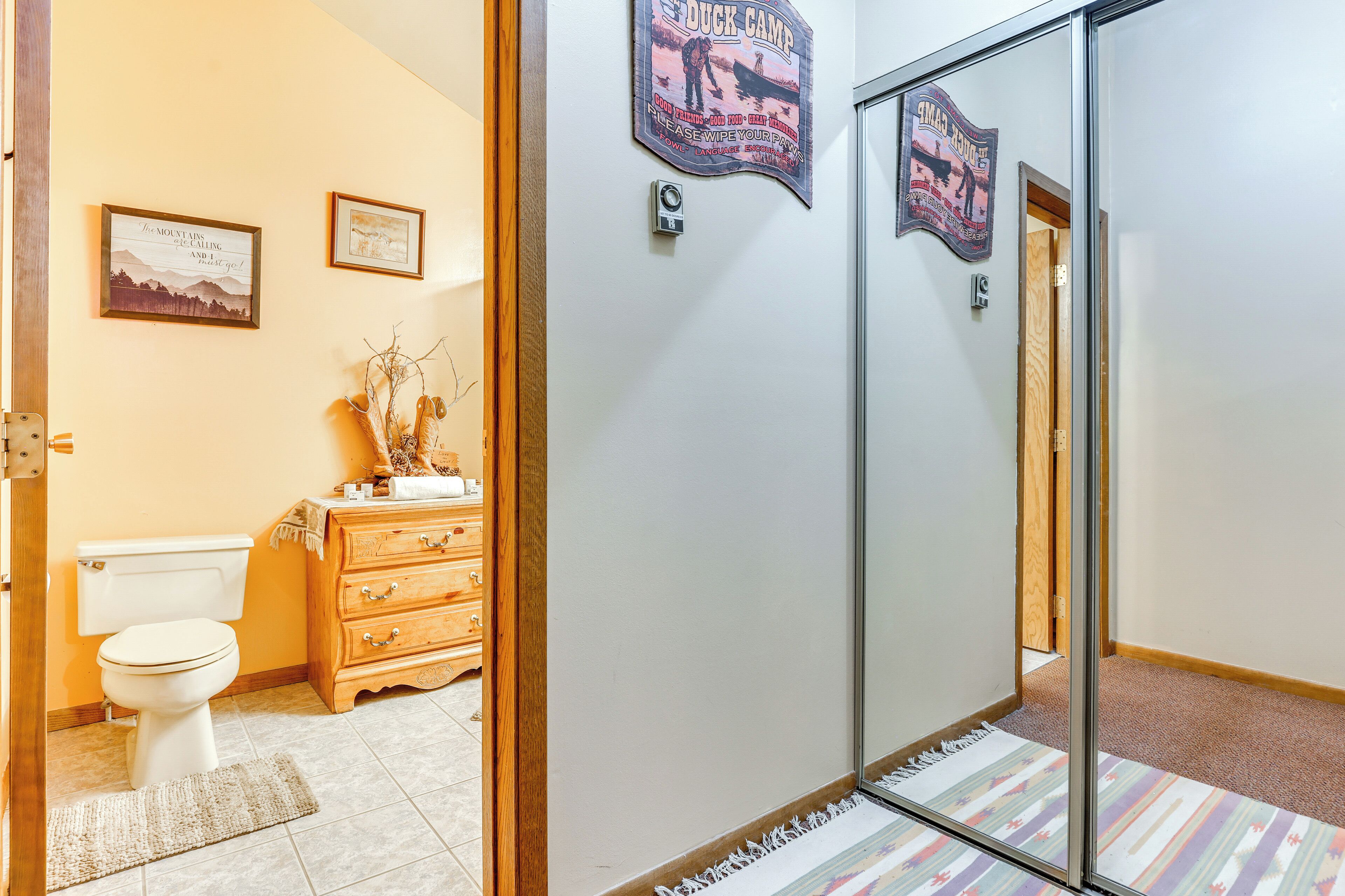 A bathroom with a toilet, wooden dresser, and framed pictures on the wall.