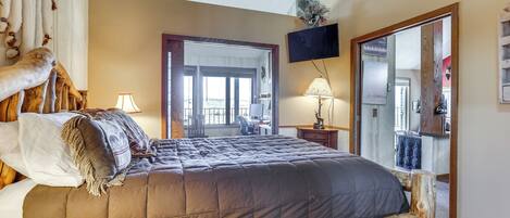 A bedroom with a large bed, a wooden headboard, a TV mounted on the wall, and a mirror.