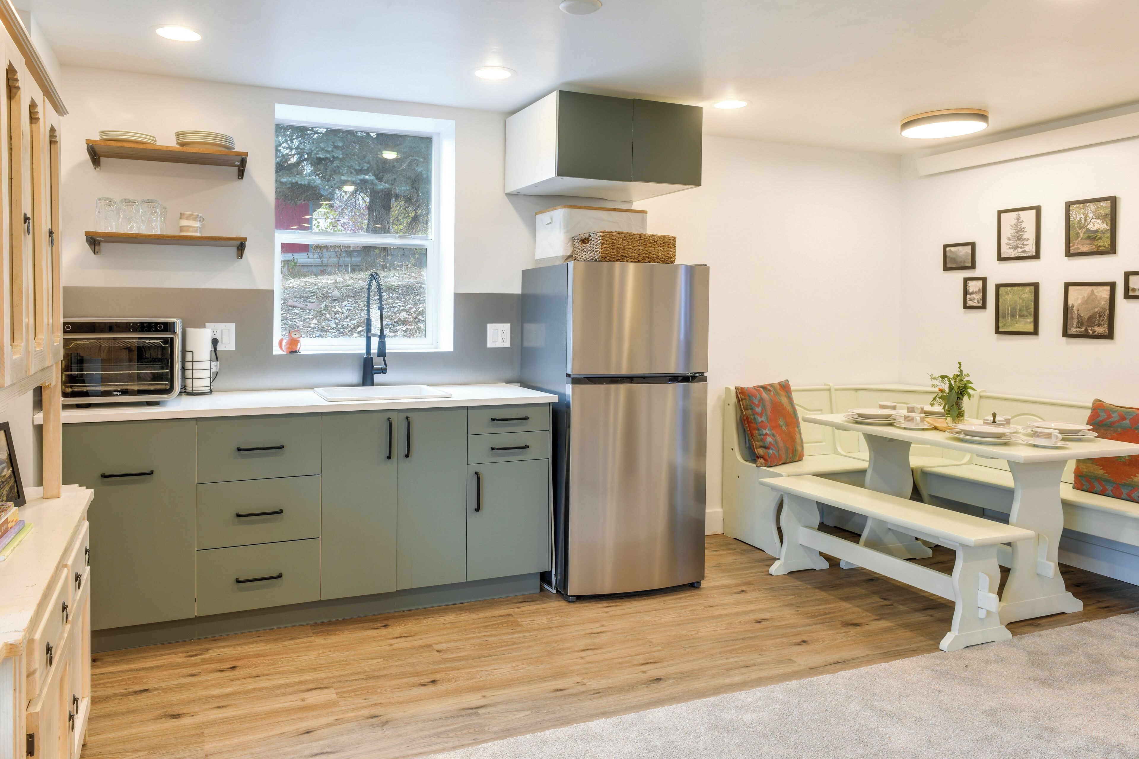 Eine moderne Küche mit einem Edelstahl-Kühlschrank, Holzböden, einem eingebauten Backofen und einem Fenster, das für natürliches Licht sorgt.